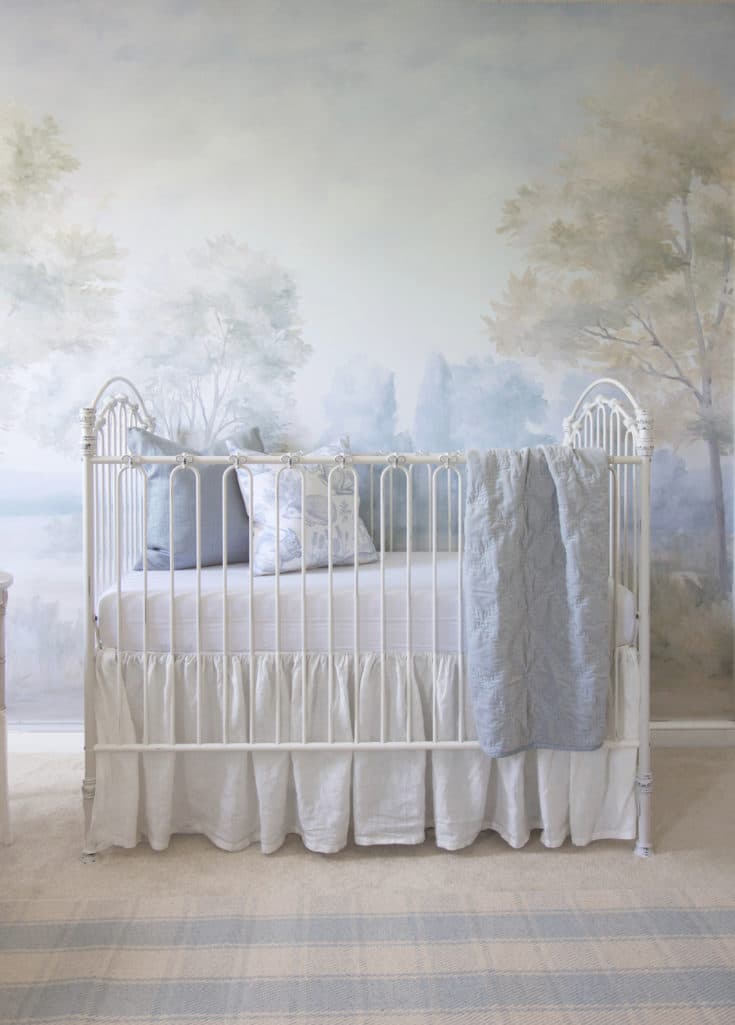 Light blue nursery crib with scenic mural wallpaper