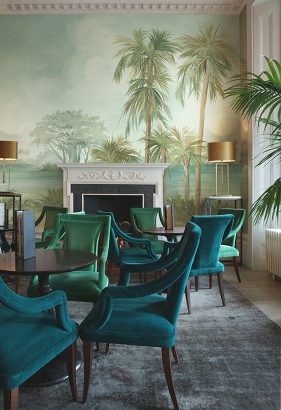 elegant english dining hall restaurant with teal and green chairs and a tropical beach mural wallpaper over the fireplace