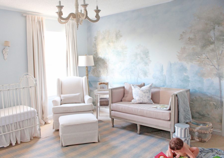 elegant nursery with pink sofa and a blue hue painterly mural landscape wallpaper and a chandelier